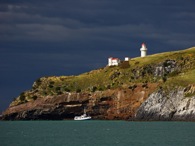 Taiaroa Head with lighthouse, small boat, and dark clouds