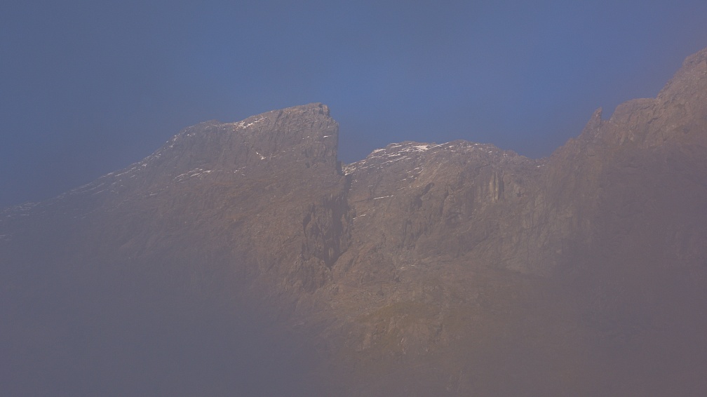 Sunlit mountain face through fog